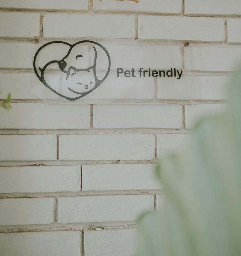 A close-up of a pet friendly sign on a white brick wall, featuring a heart with a dog and cat illustration.